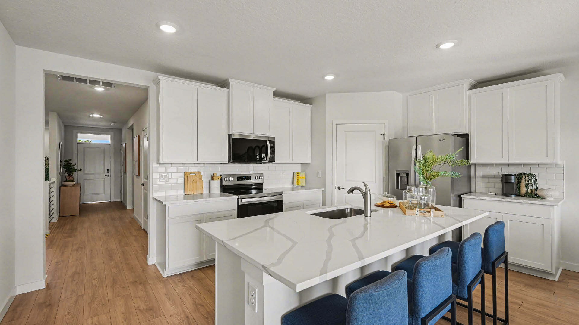 Modern kitchen with white cabinetry, stainless steel appliances, and a large island with seating. Bright and welcoming entryway visible.