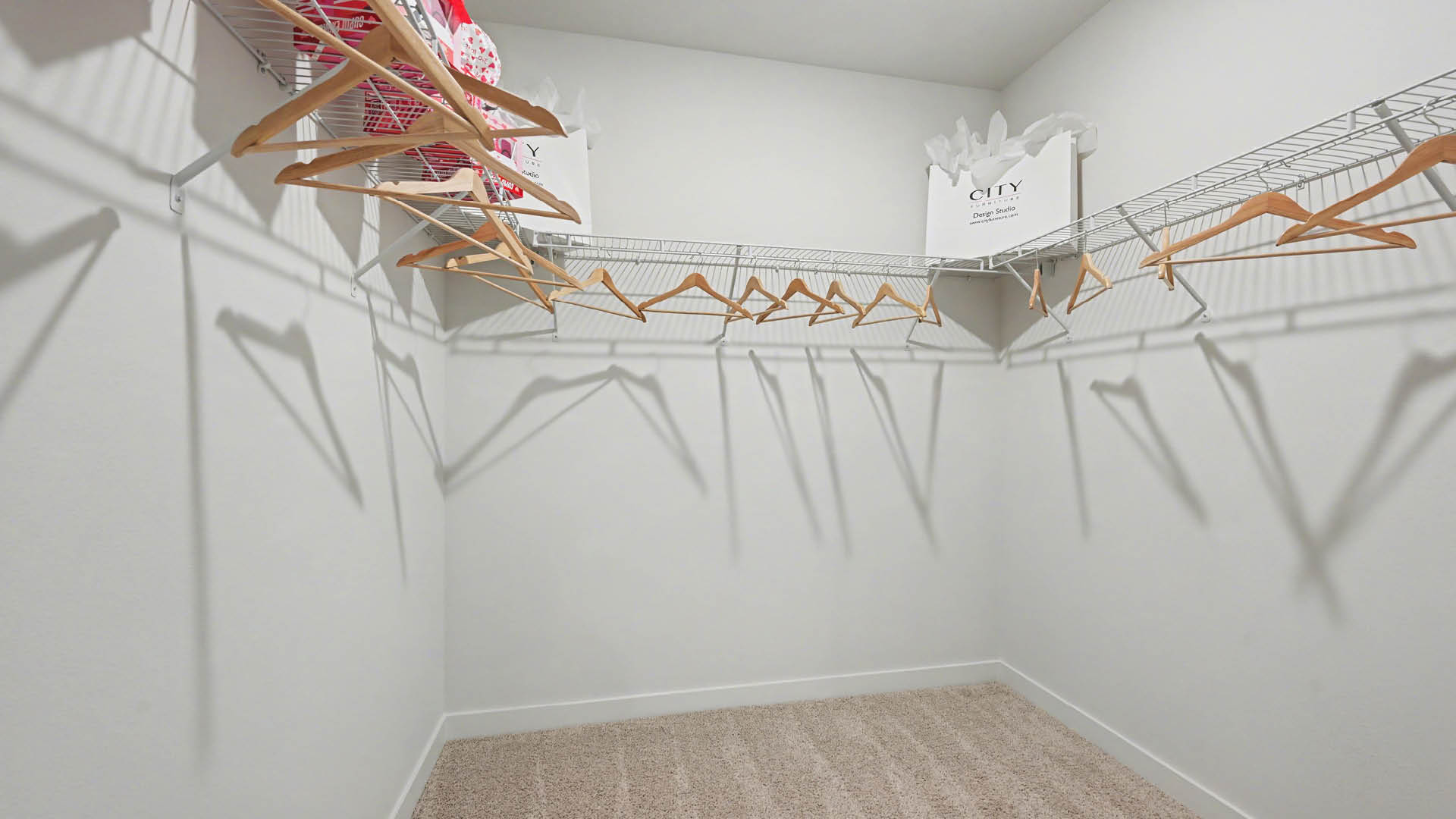 A spacious, empty closet featuring white wire shelves with wooden clothes hangers, against a light-colored wall.