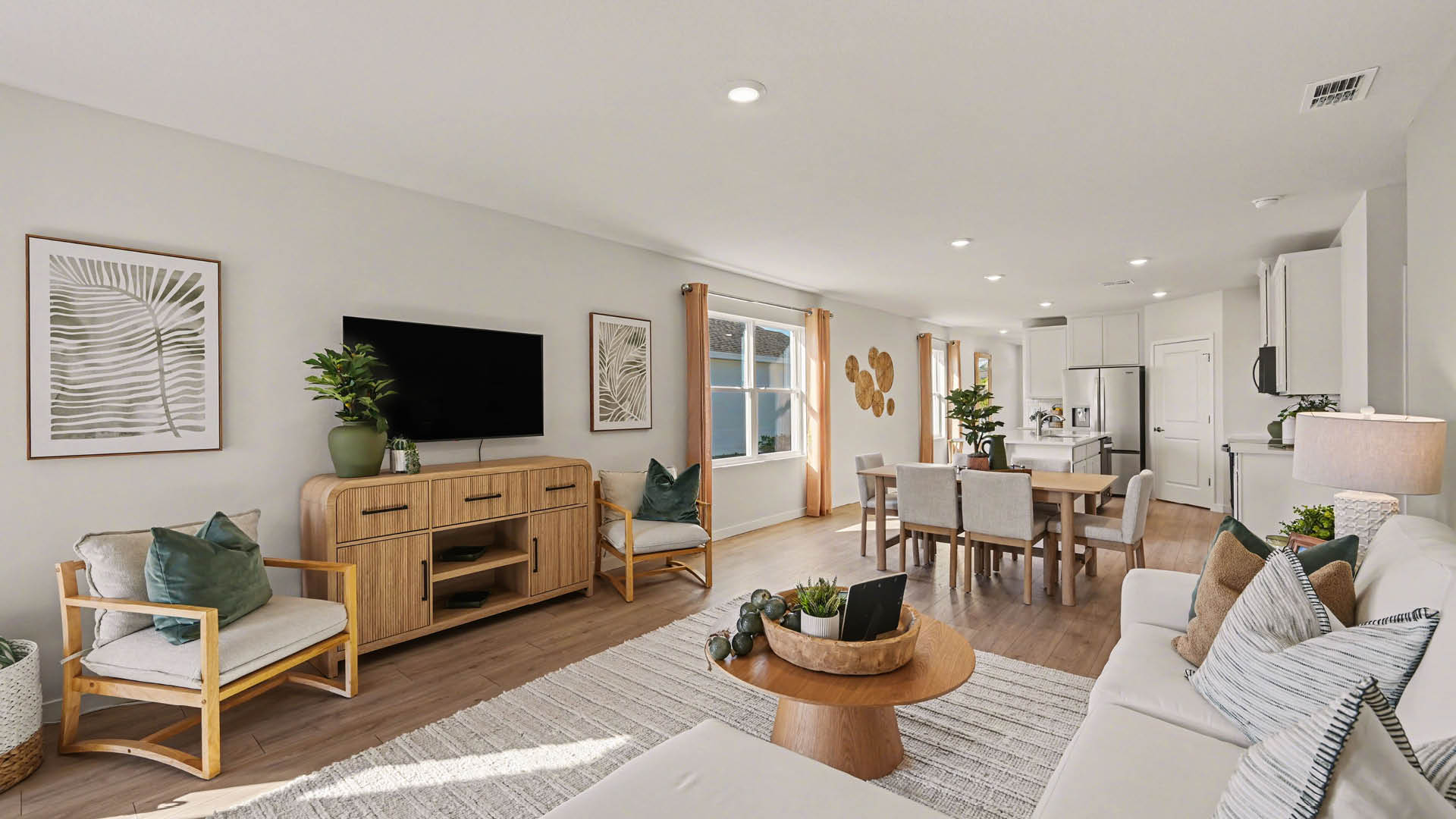 A spacious living room, leading into a dining and kitchen area. There are several windows along the walls and Mohawk® Revwood Select Plank Flooring throughout.