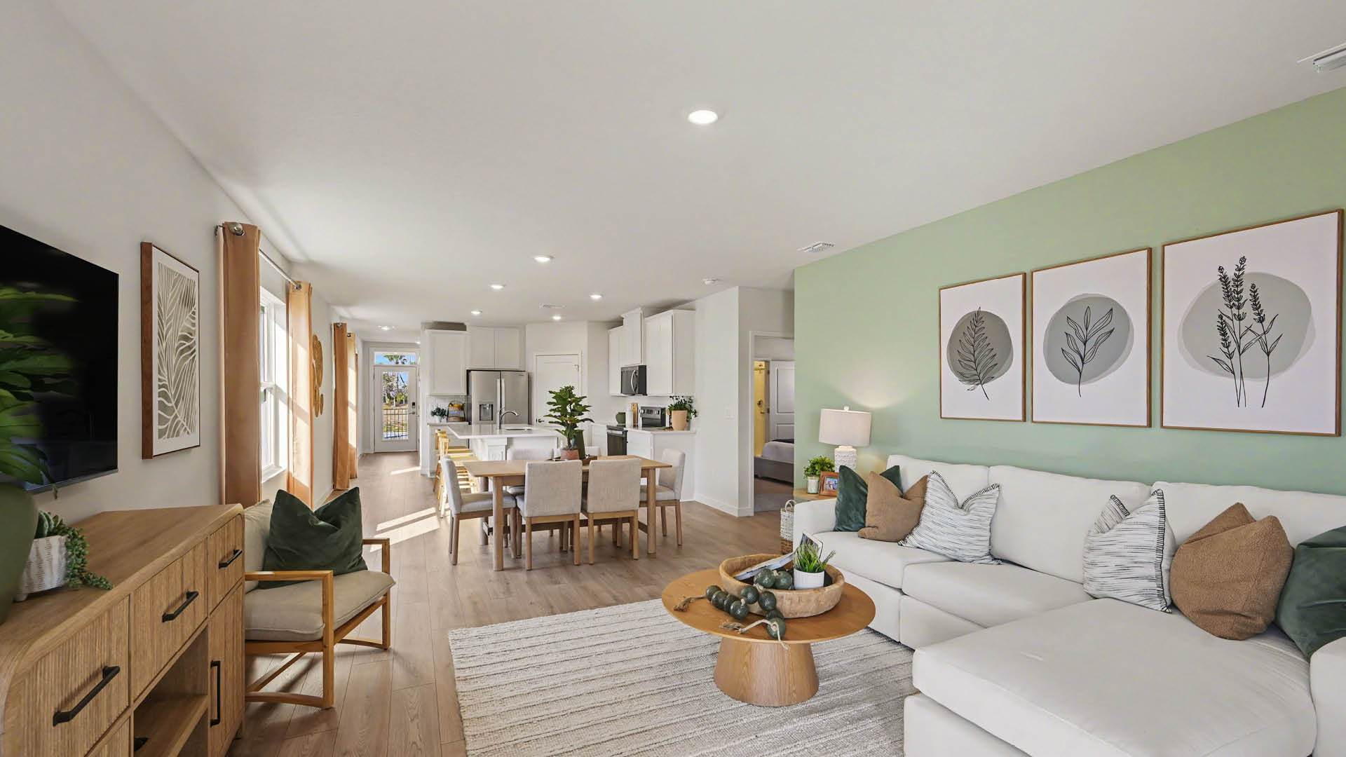 A spacious living room, leading into a dining and kitchen area. There are several windows along the walls and Mohawk® Revwood Select Plank Flooring throughout.