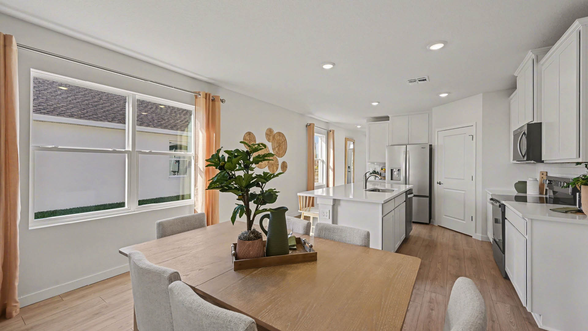 A cozy dining area with large windows leading into a modern kitchen with white cabinetry, stainless steel appliances, and a large island with seating.