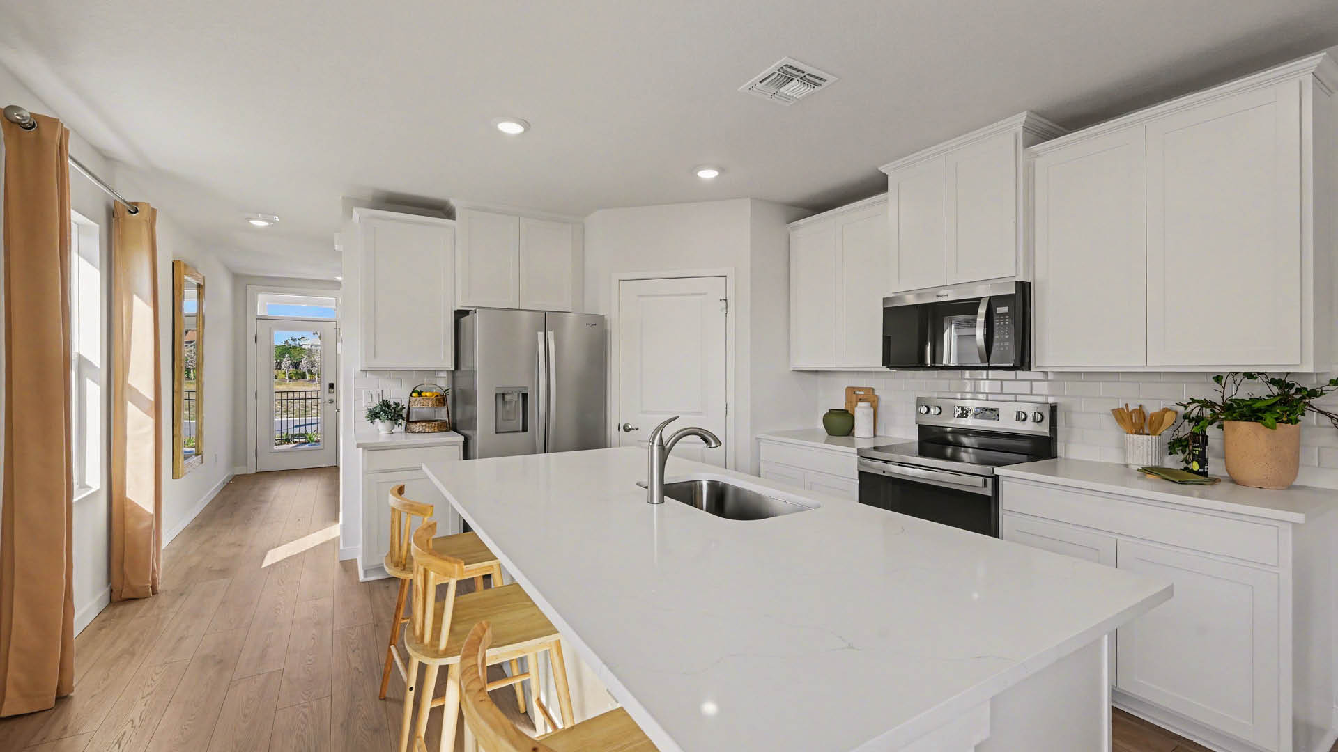 A large kitchen with quartz countertops, stainless steel appliances, and a center island with seating. An entryway hallway leading to the front door is visible.