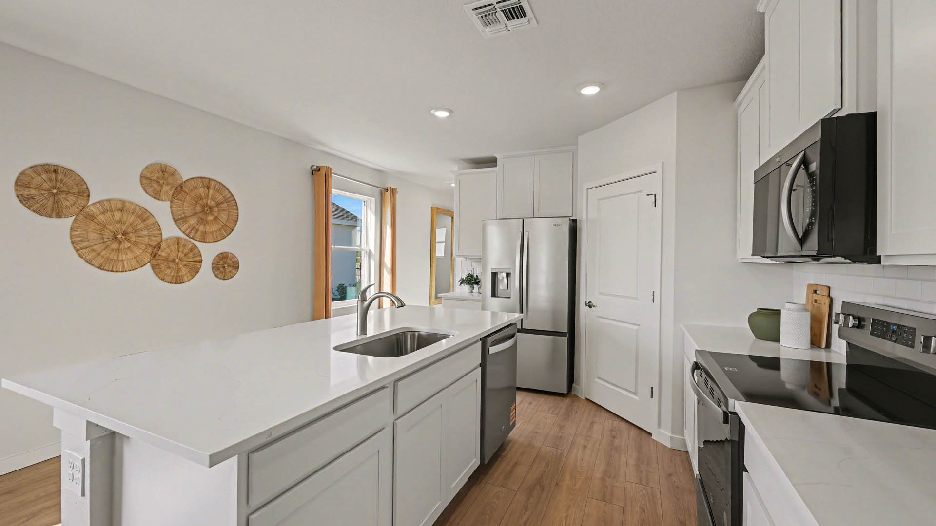 A large kitchen with quartz countertops, stainless steel appliances, and a center island with seating. A large window lets in natural light.