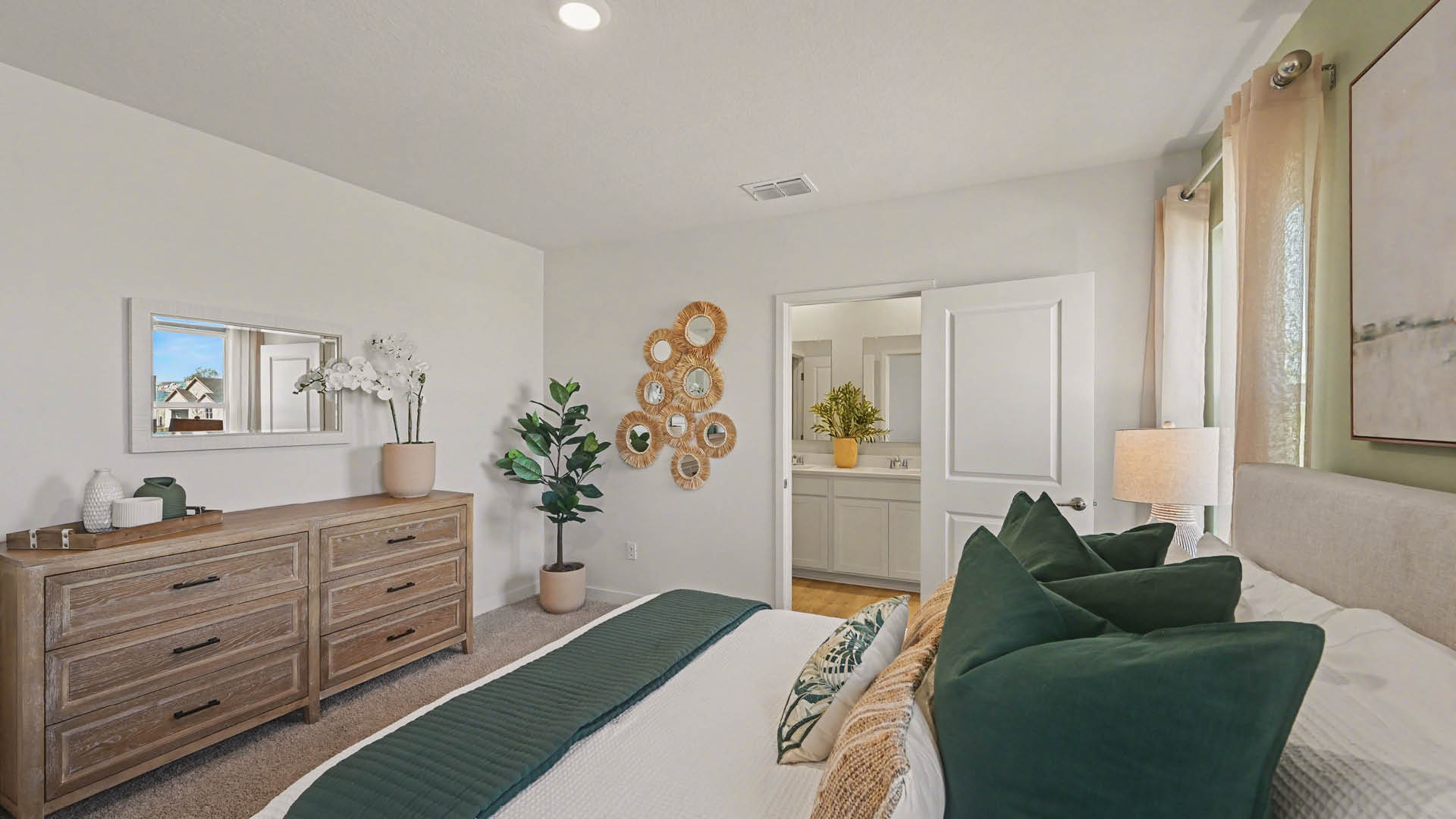 A large bedroom with beige carpet, white walls, and a window, allowing natural light to illuminate the space. An open door leading to an ensuite bathroom is visible.