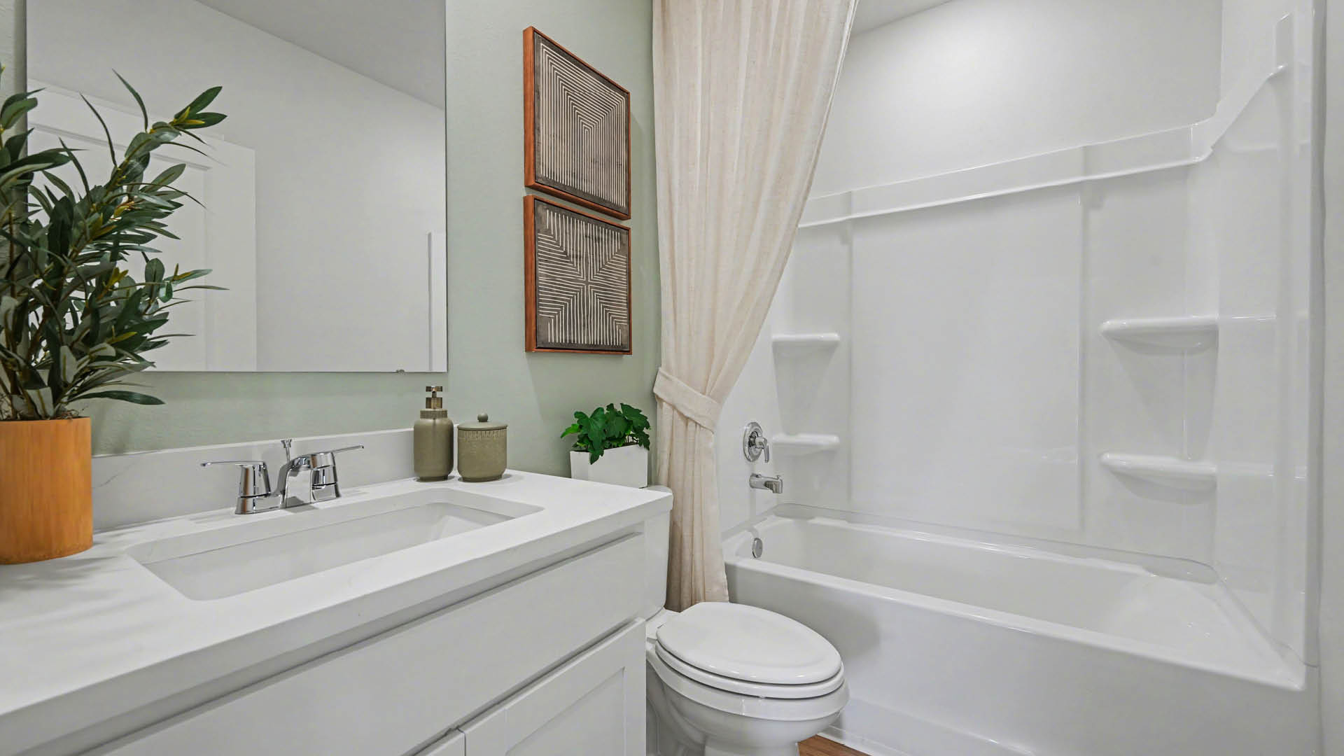 A clean, modern bathroom featuring quartz countertops, a bathtub with a shower, and a large mirror against neutral-colored walls.