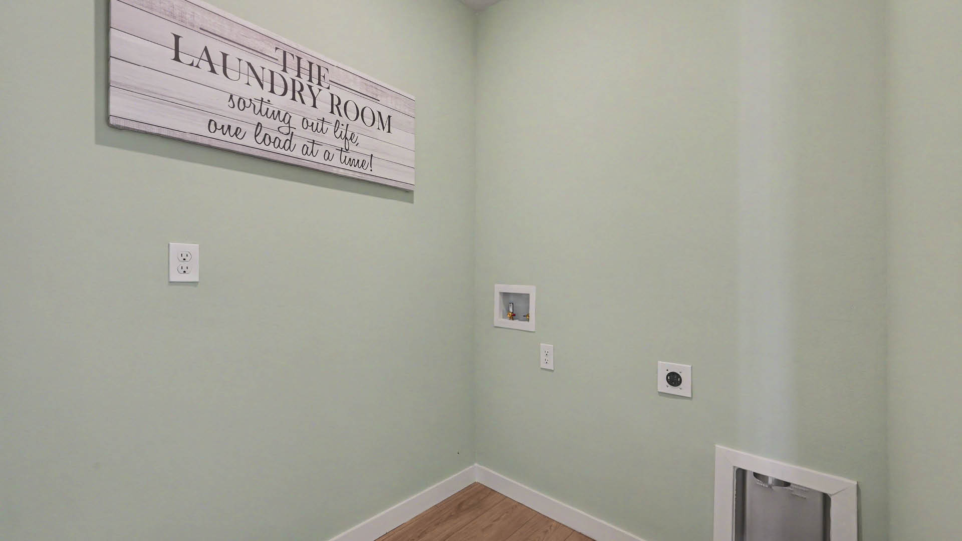 A laundry room with utility connections on the wall and Mohawk® Revwood Select Plank Flooring.
