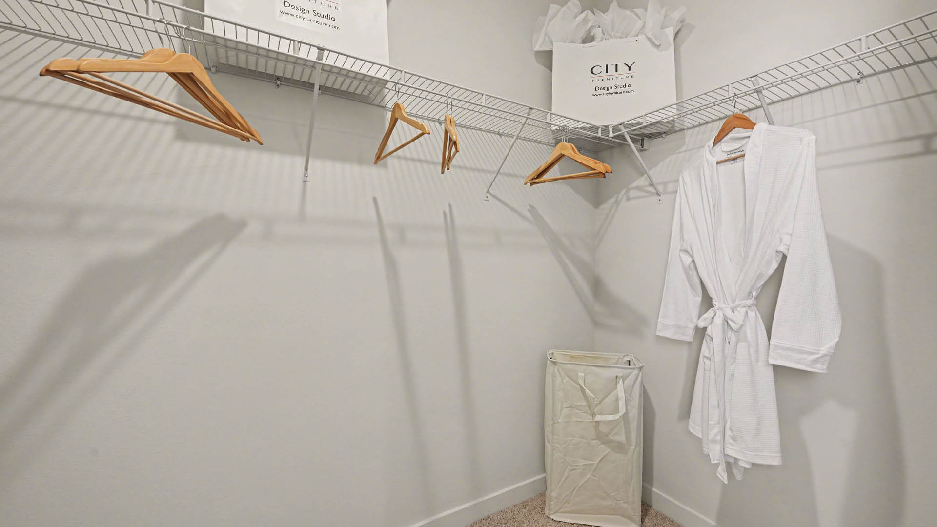 A spacious, walk-in closet featuring white wire shelves with wooden clothes hangers, against a light-colored wall. A white robe hangs on a rack in a closet.