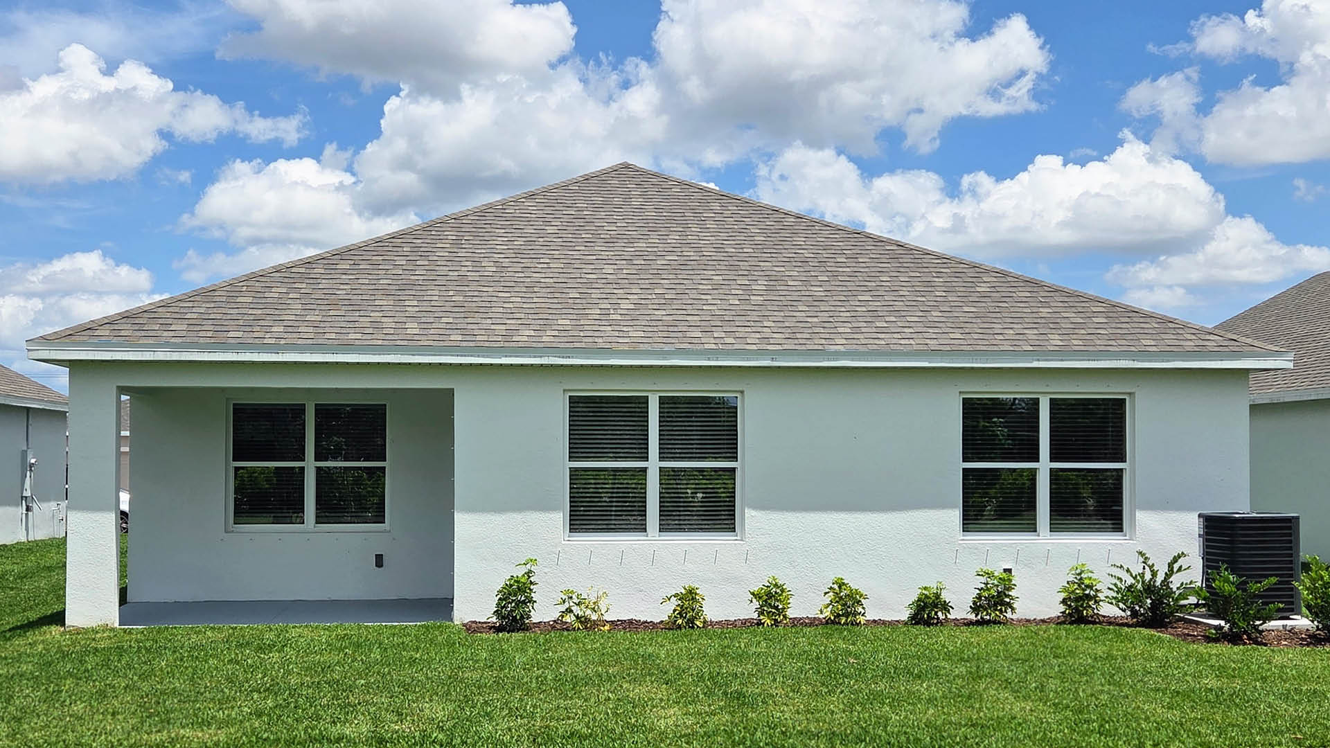 A photo showing the rear view of a home with a stucco exterior and covered patio.