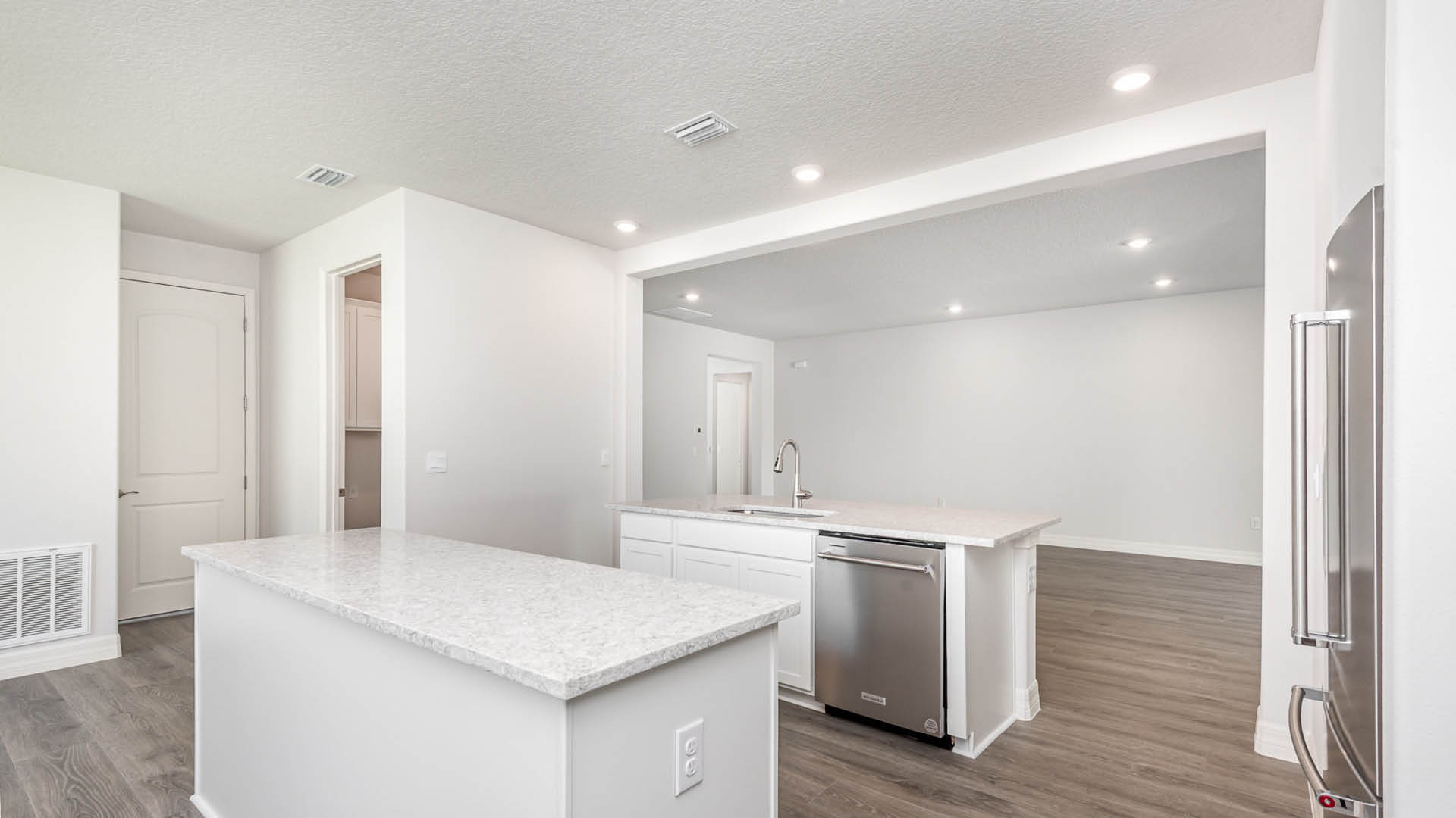 Bright, modern kitchen featuring white cabinetry, a large island with a quartz countertop, and stainless-steel appliances, with open layout.