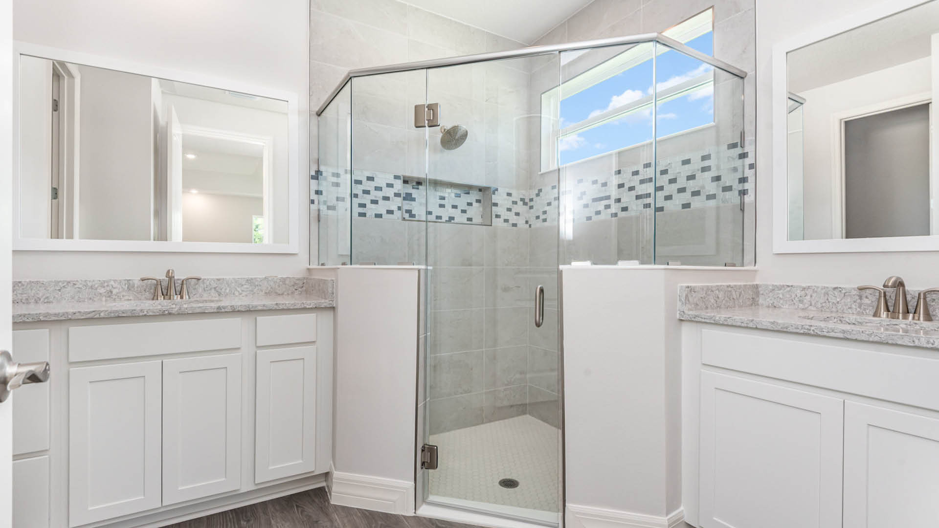 Modern bathroom featuring a glass shower, dual sinks with quartz countertops, large mirrors, and neutral tile accents. Bright and airy ambiance.