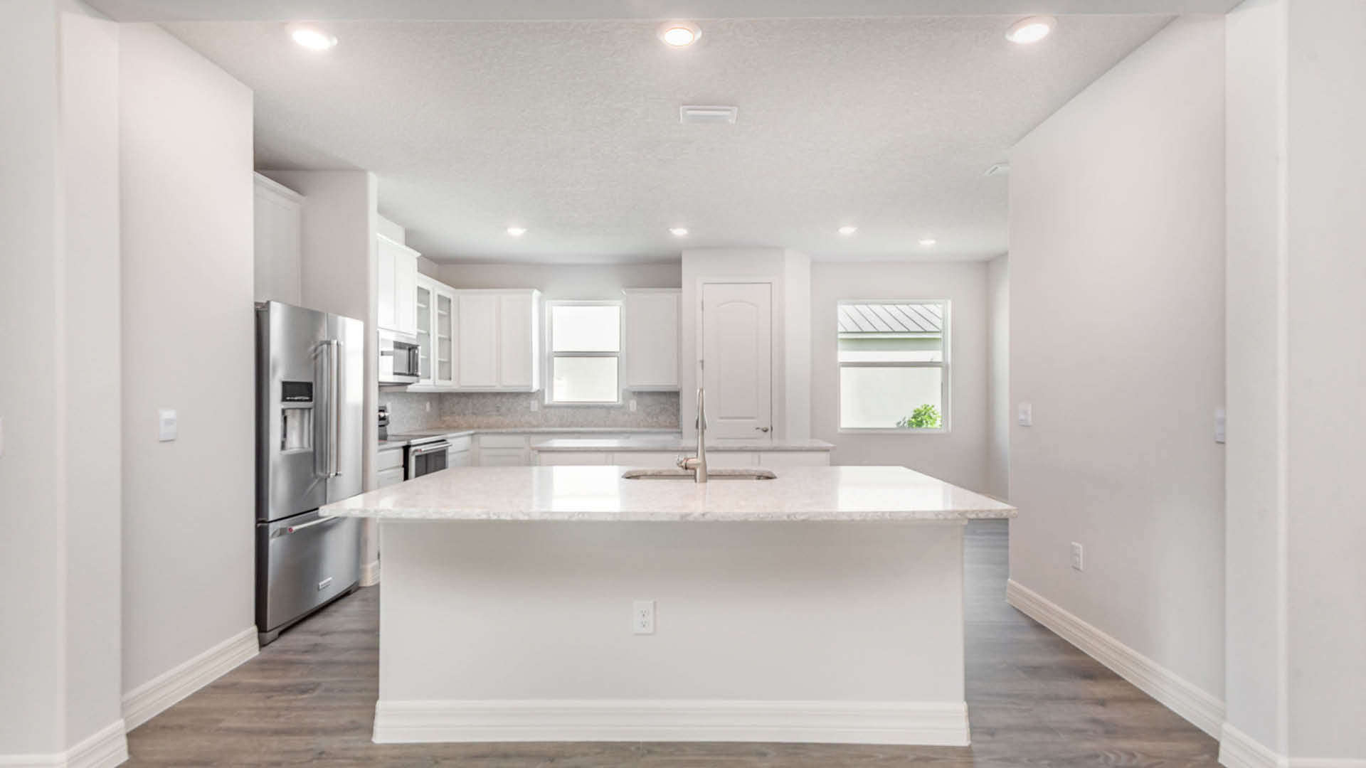 Modern kitchen with white cabinetry, stainless steel appliances, and a spacious island, featuring quartz countertops and bright lighting.
