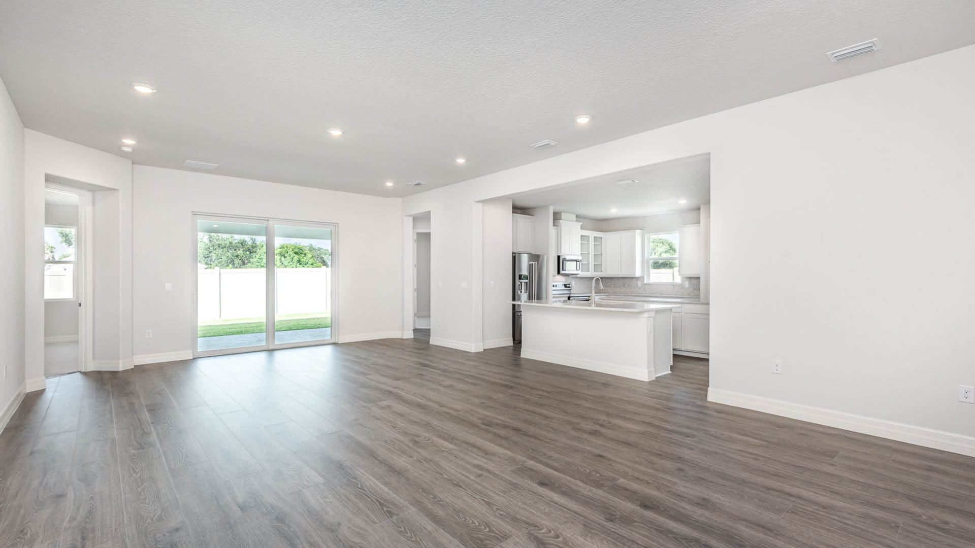 Spacious, modern living area with sleek vinyl plank floors, white walls, and a view of the backyard through sliding glass doors.