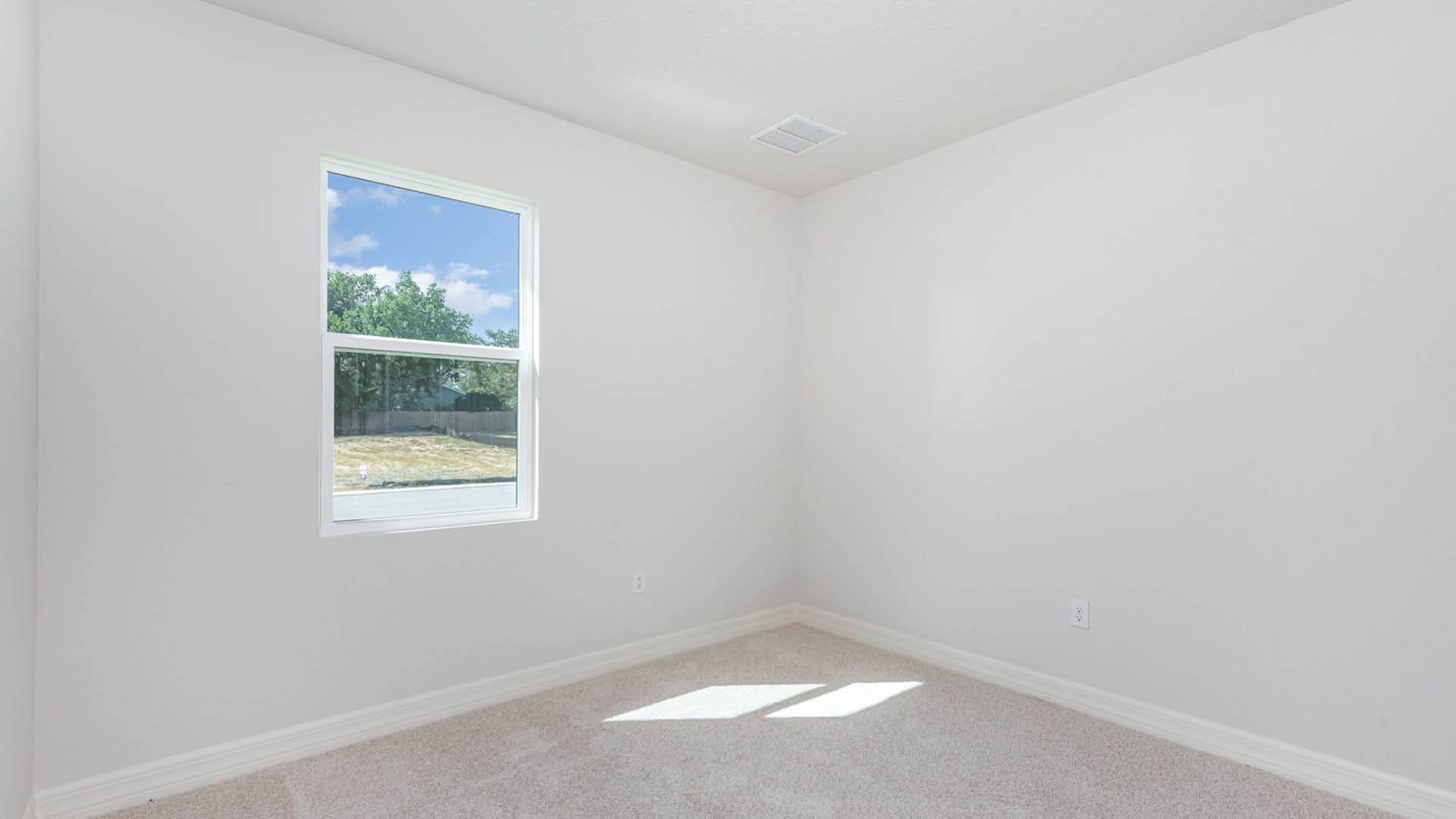 An empty room featuring a window and a carpeted floor, with soft natural light illuminating the space.