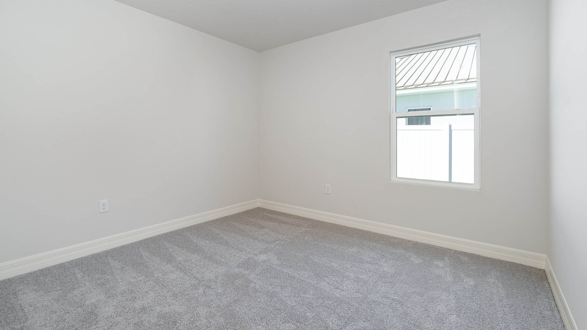 An empty room with beige carpet, white walls, and a window, allowing natural light to illuminate the space.