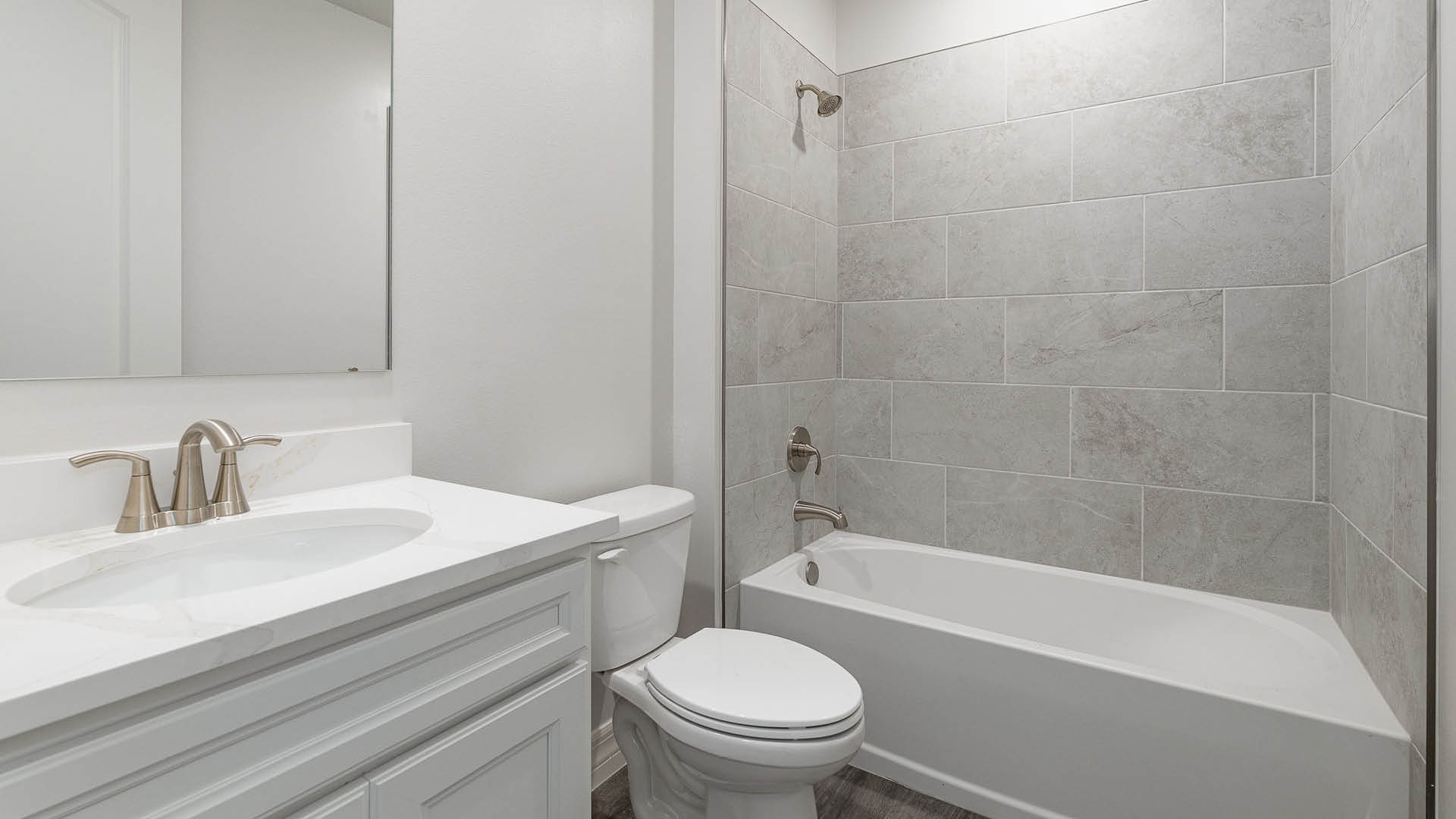 A clean, modern bathroom featuring quartz countertops, a bathtub with a shower, and a large mirror against neutral-colored walls.