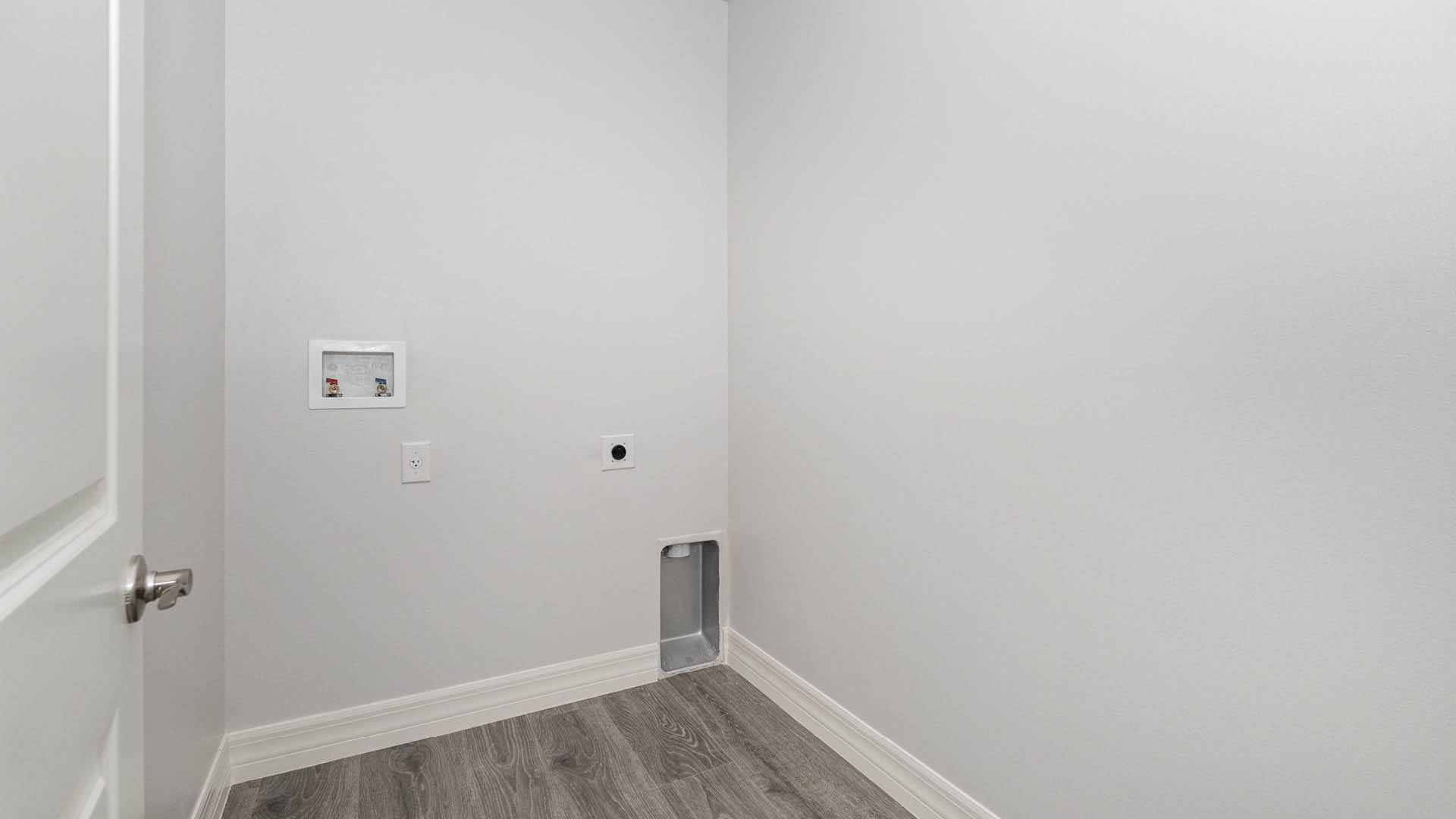 A laundry room with utility connections on the wall and Mohawk® Revwood Select Plank Flooring.