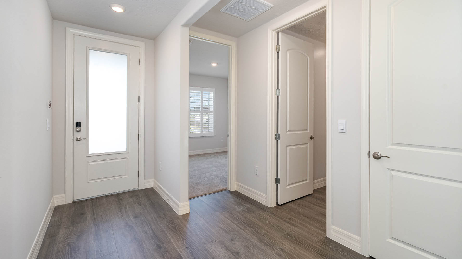 A bright entryway hallway with Mohawk® Revwood Select Plank Flooring, featuring a closed front door, a closed hall door, and two open doors leading elsewhere.