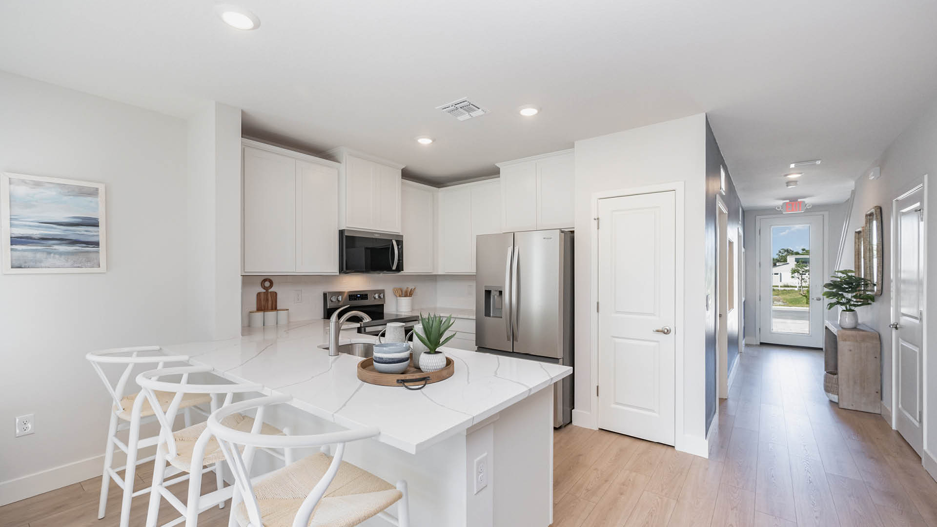 Modern kitchen featuring white cabinets, stainless steel appliances, and a quartz-topped island with seating and decorative accents.