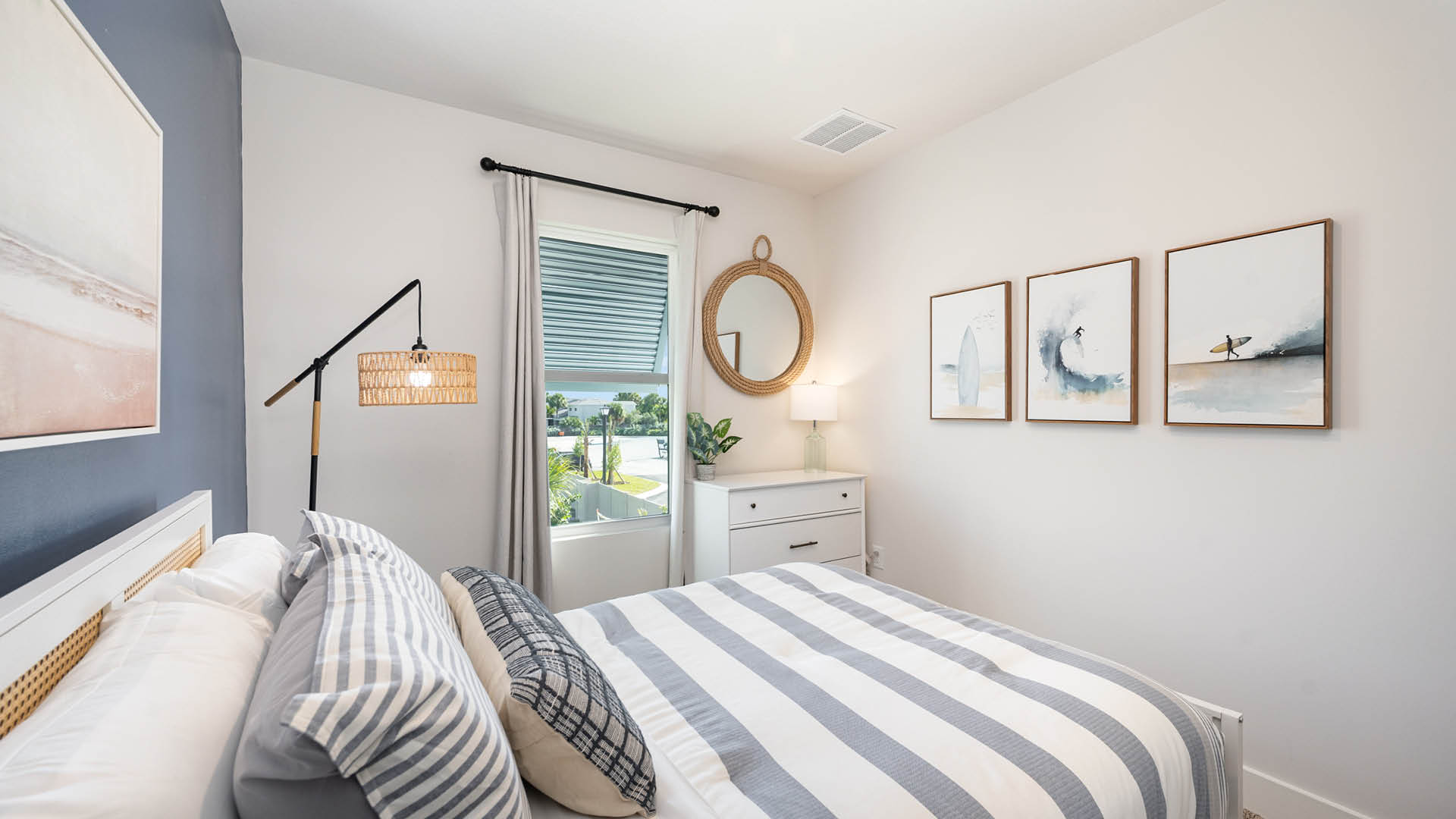 Coastal bedroom with white bed, blue accent wall and large window.