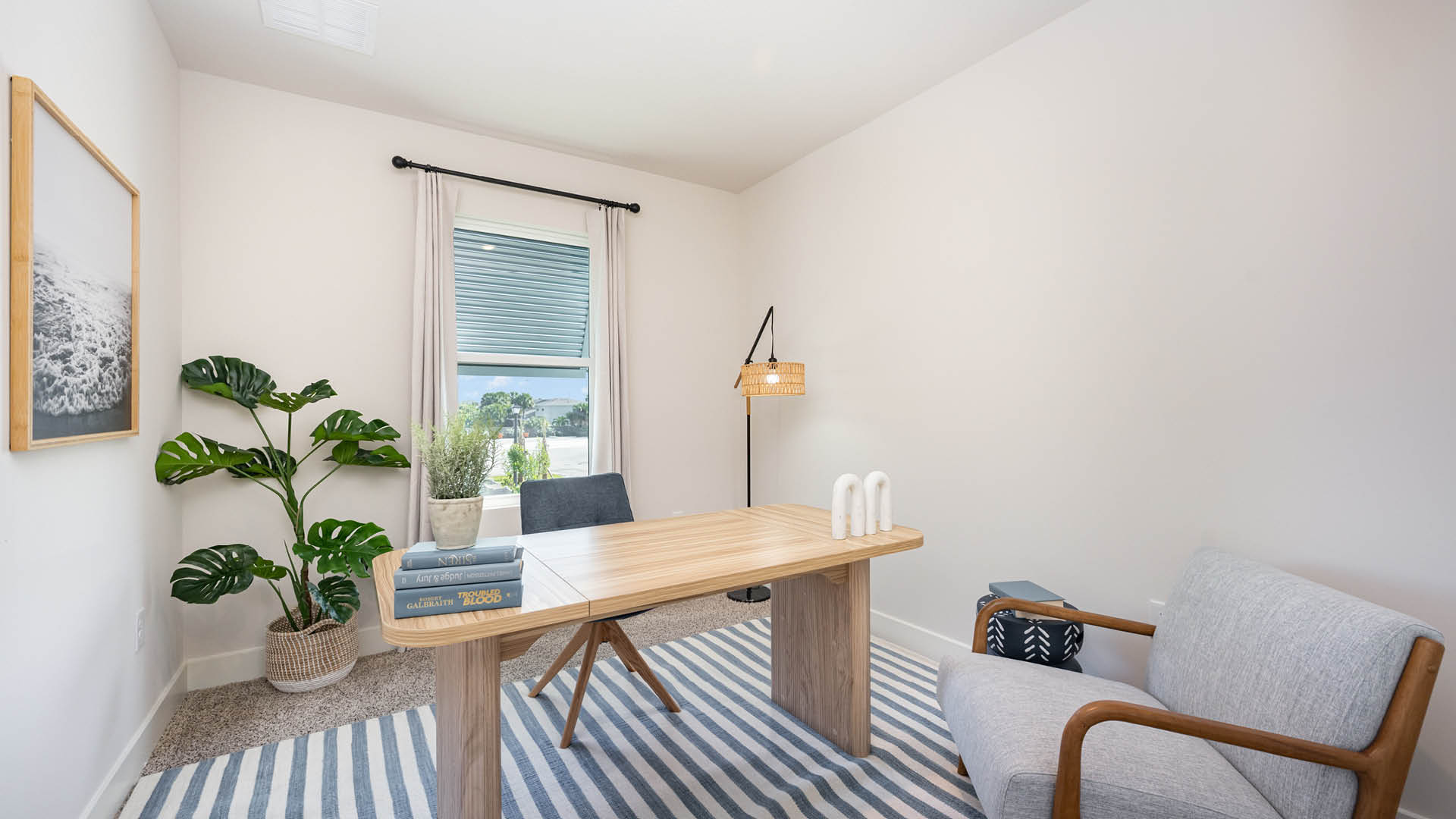 Cozy home office with blue desk chair, light wood tone desk and large window.