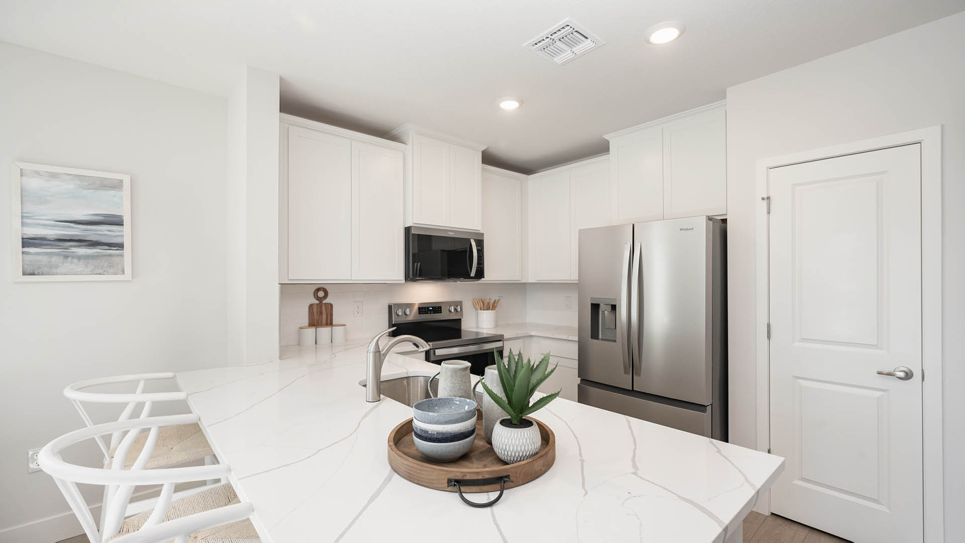 Bright white kitchen with quartz countertops and stainless steel appliances.