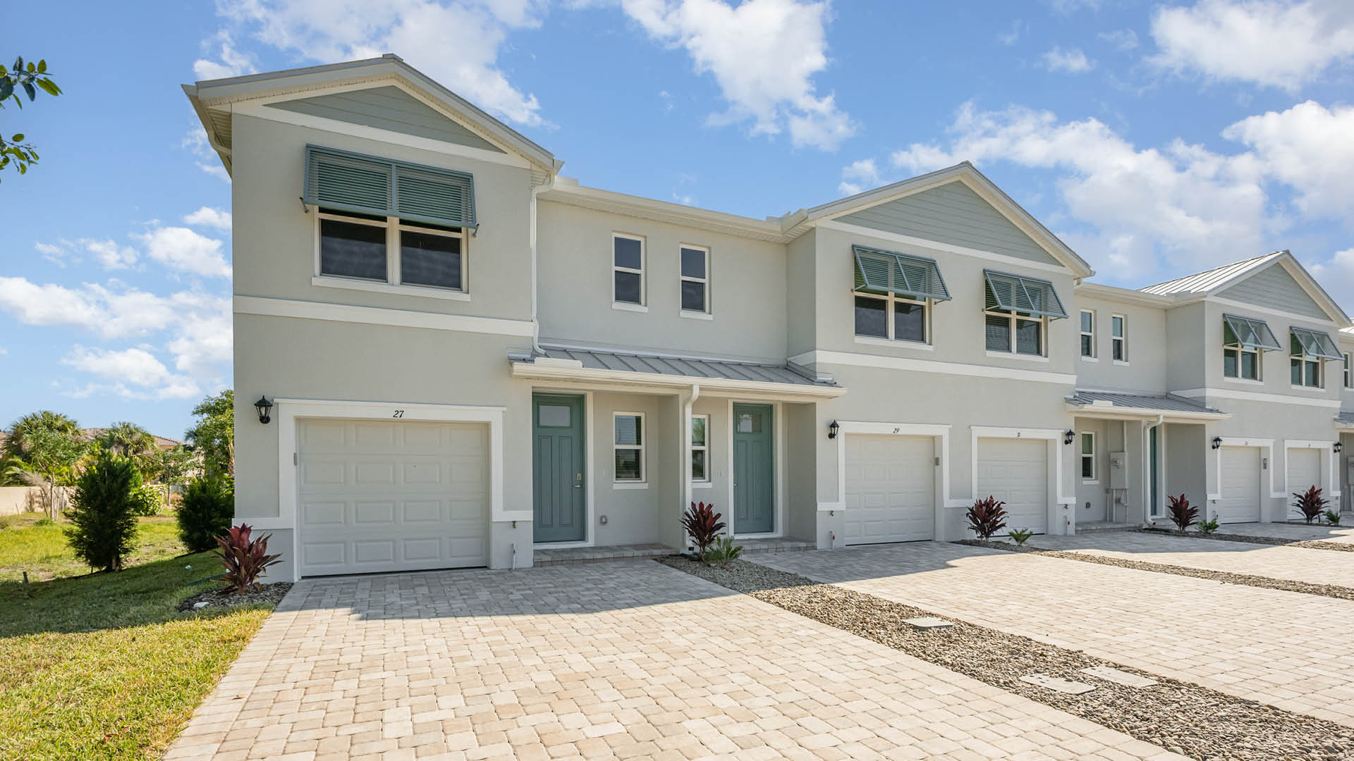 Modern Townhome with grey exterior, blue bahamian shutters, one car garage and paver driveway.