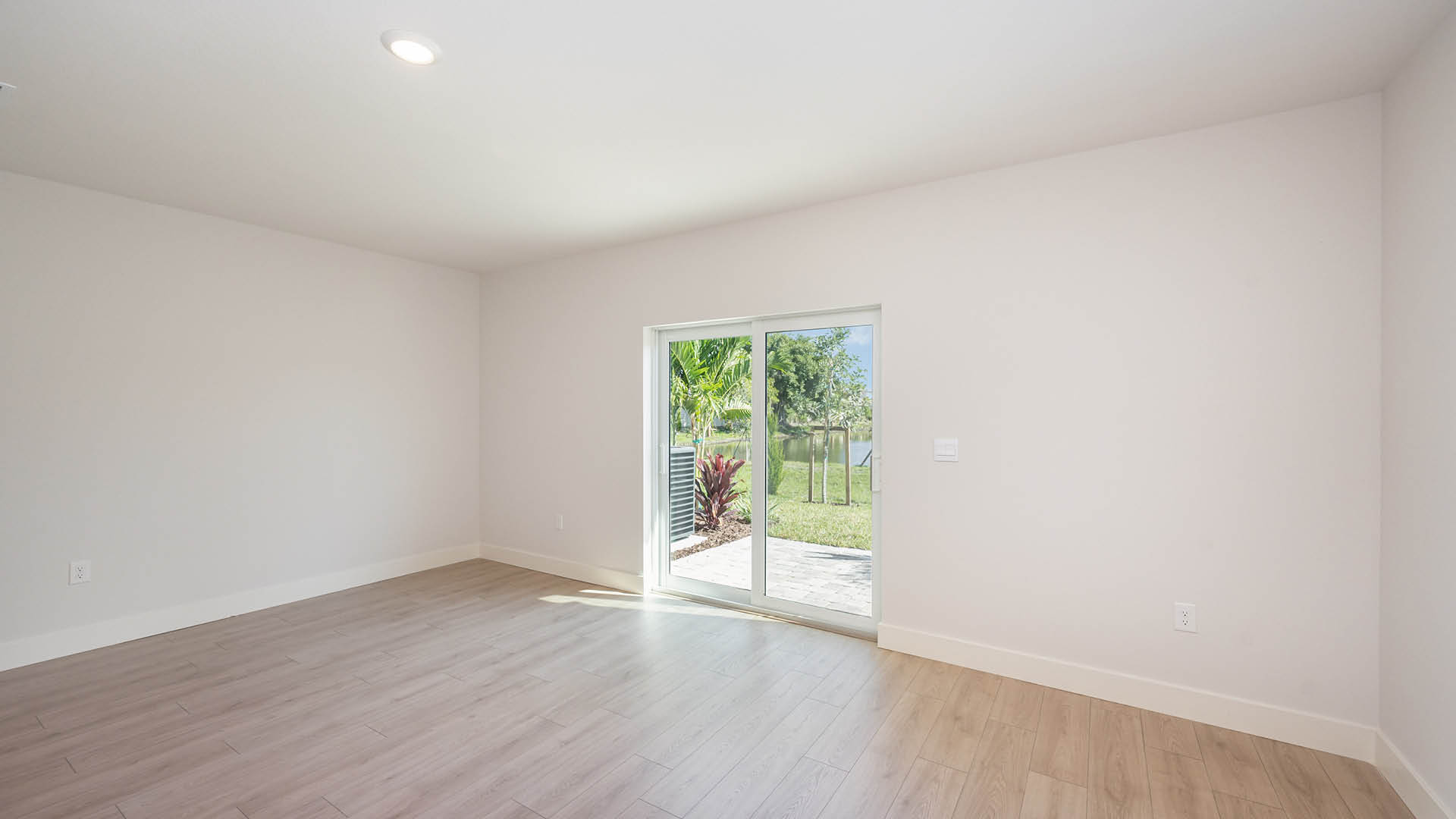 4. Spacious, modern living area featuring light wood flooring.5. Rear view of a townhouse featuring a white stucco exterior, sliding glass door, and a well-kept lawn.	4. Spacious, modern living area featuring light wood flooring.