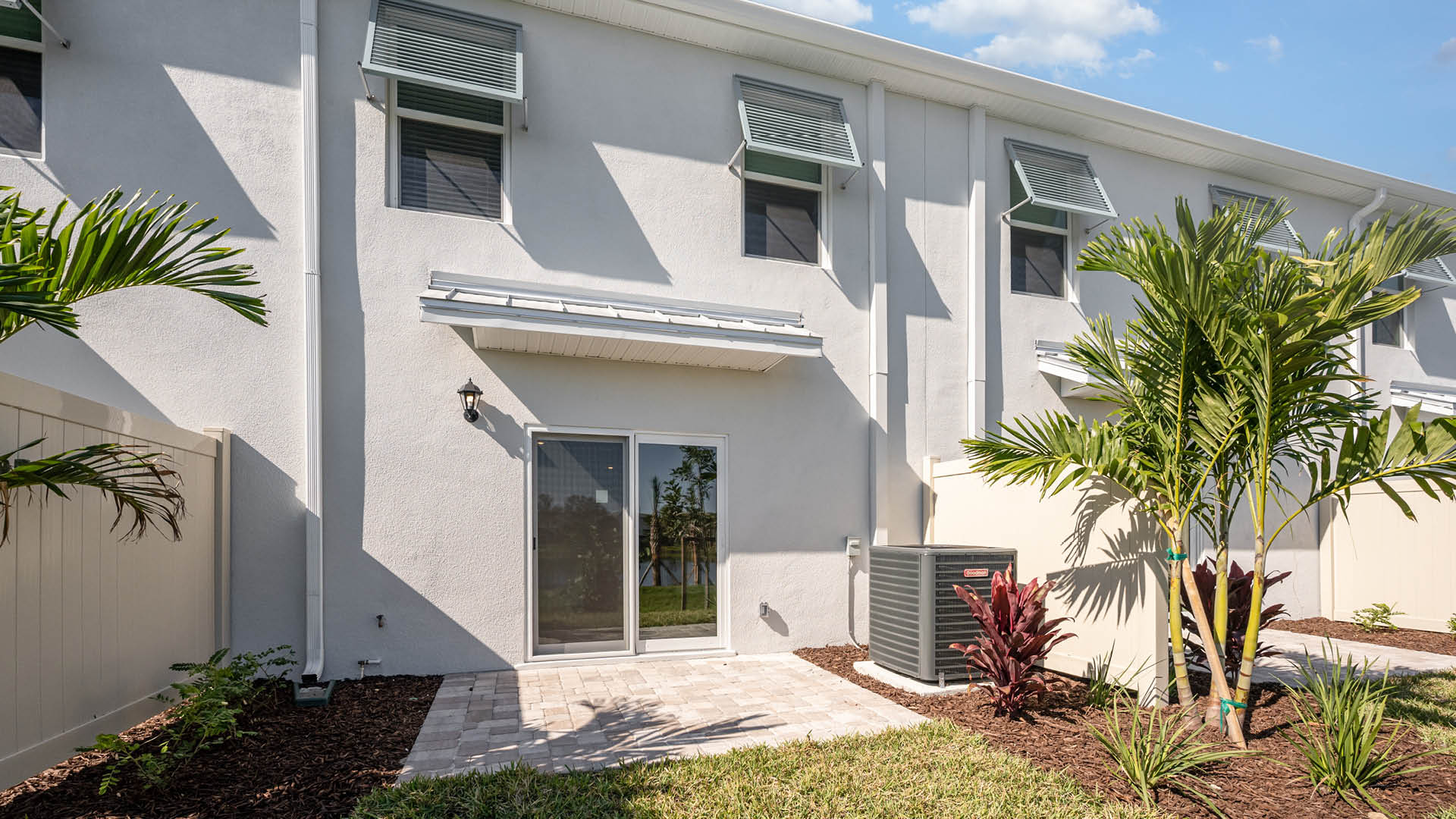 Rear view of a townhouse featuring a white stucco exterior, sliding glass door, and a well-kept lawn.