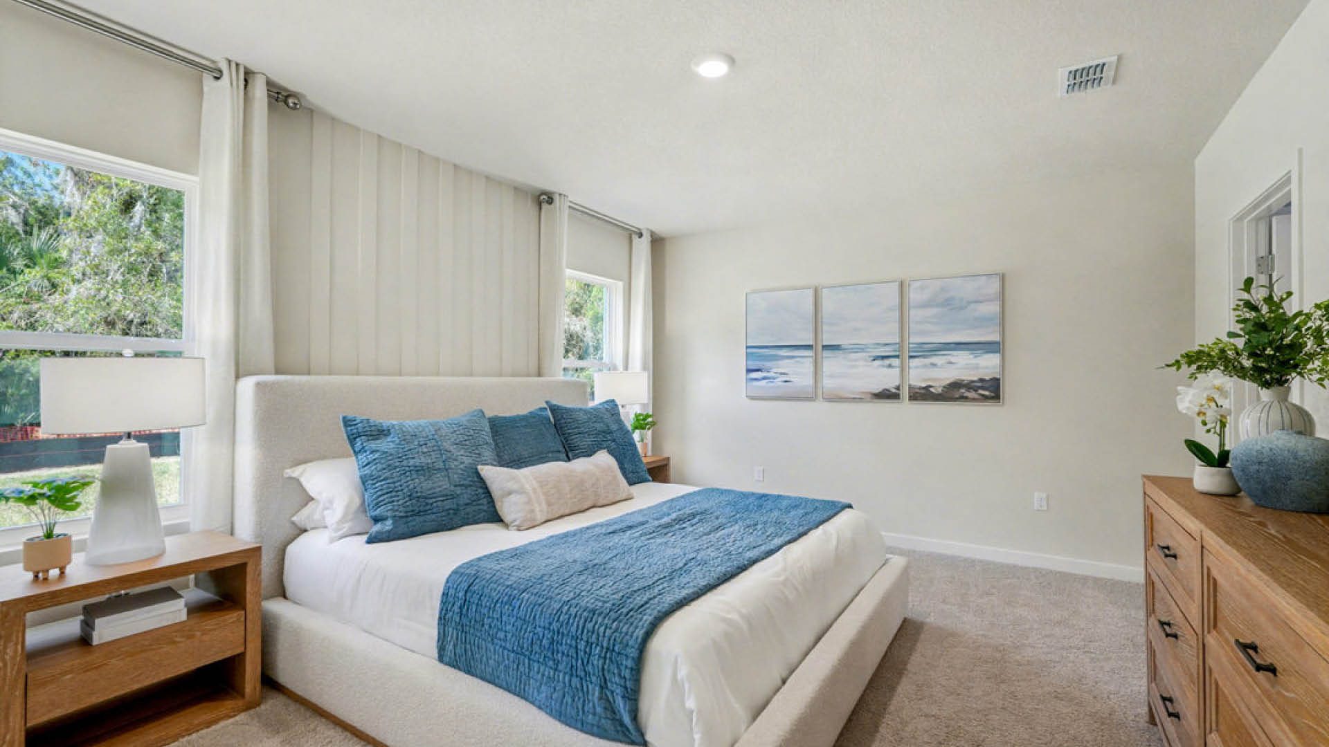 A cozy bedroom featuring a blue and white bed, complemented by soft lighting and neutral-colored walls.