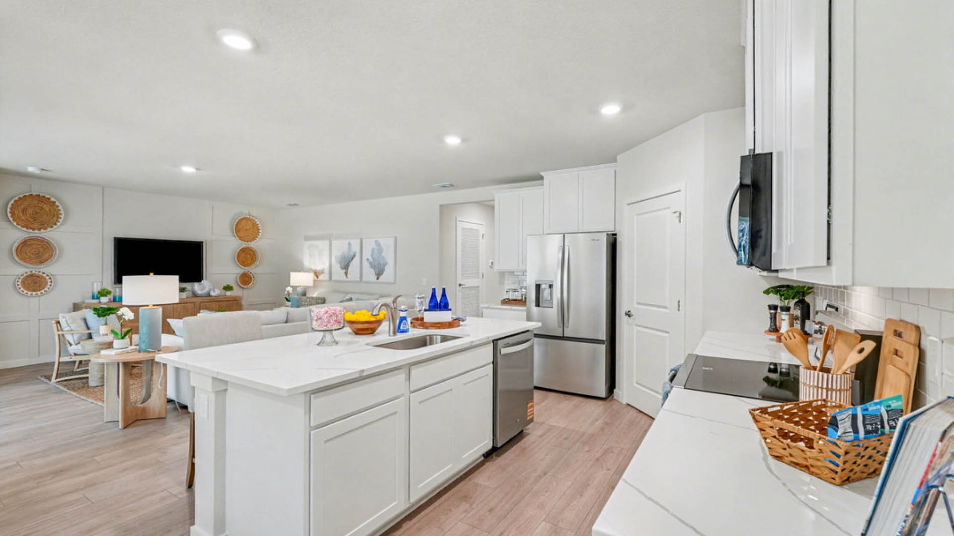 Modern kitchen with white cabinets, stainless steel appliances, and an open layout to a cozy living area featuring light decor and wooden accents.