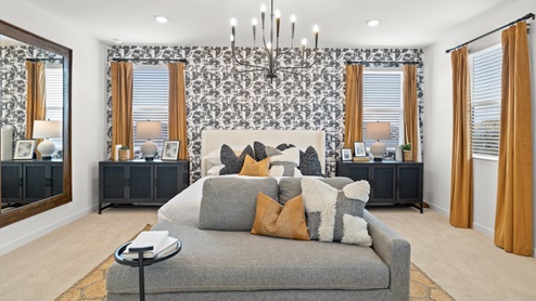 Owner's Suite with abstract accent wall, vintage yellow drapes, two large black nightstands on either side of the bed, and a gray lounge couch at the foot of the bed.