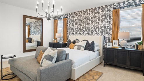 Owner's Suite with abstract accent wall, vintage yellow drapes, two large black nightstands on either side of the bed, and a gray lounge couch at the foot of the bed.