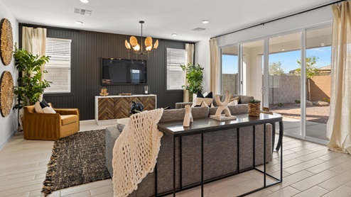 Great Room with large gray couches, full accent wall wood paneling, and large sliding doors looking out into backyard.