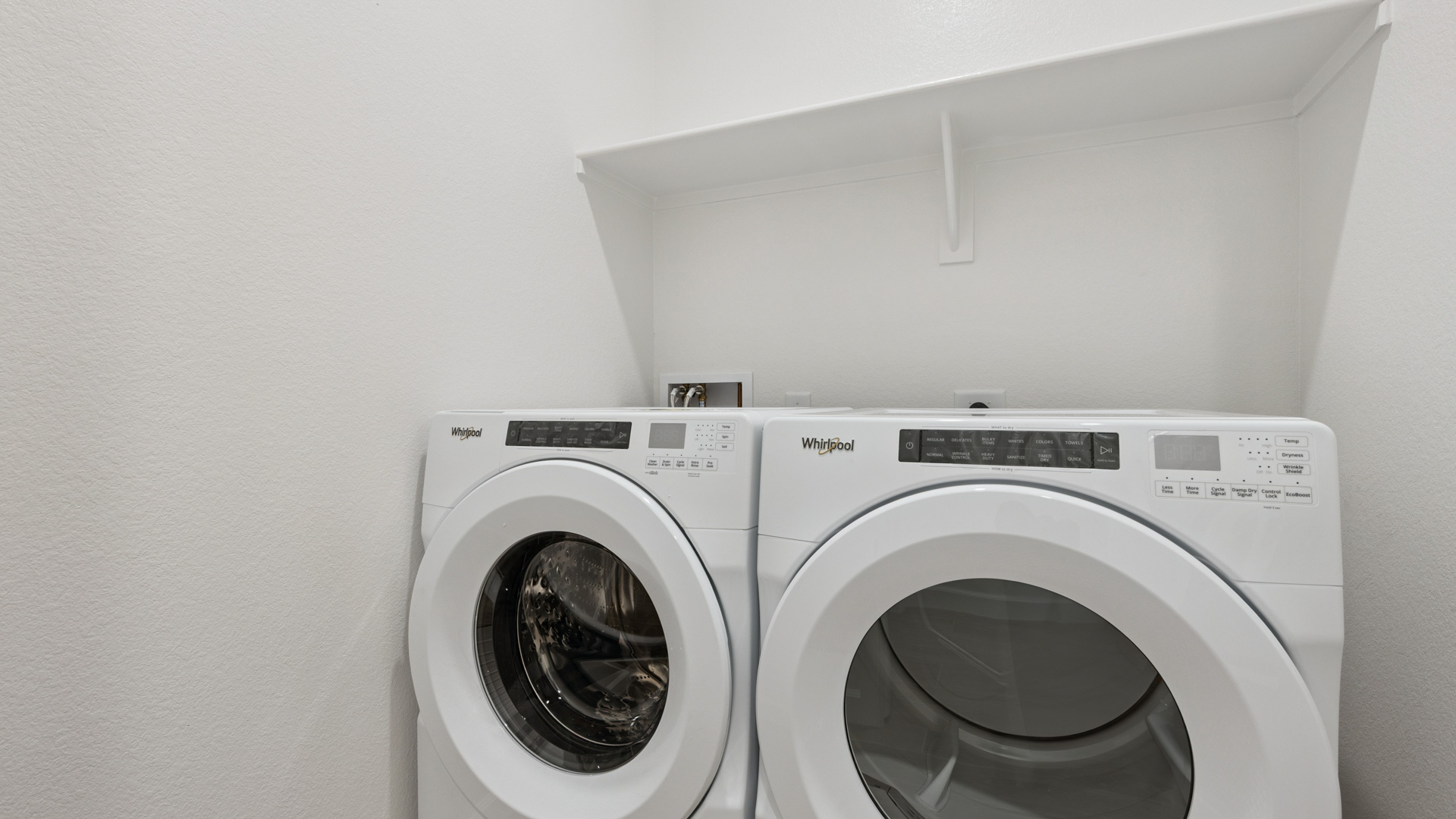 Spacious laundry room with washer and dryer connections and shelving for storage.