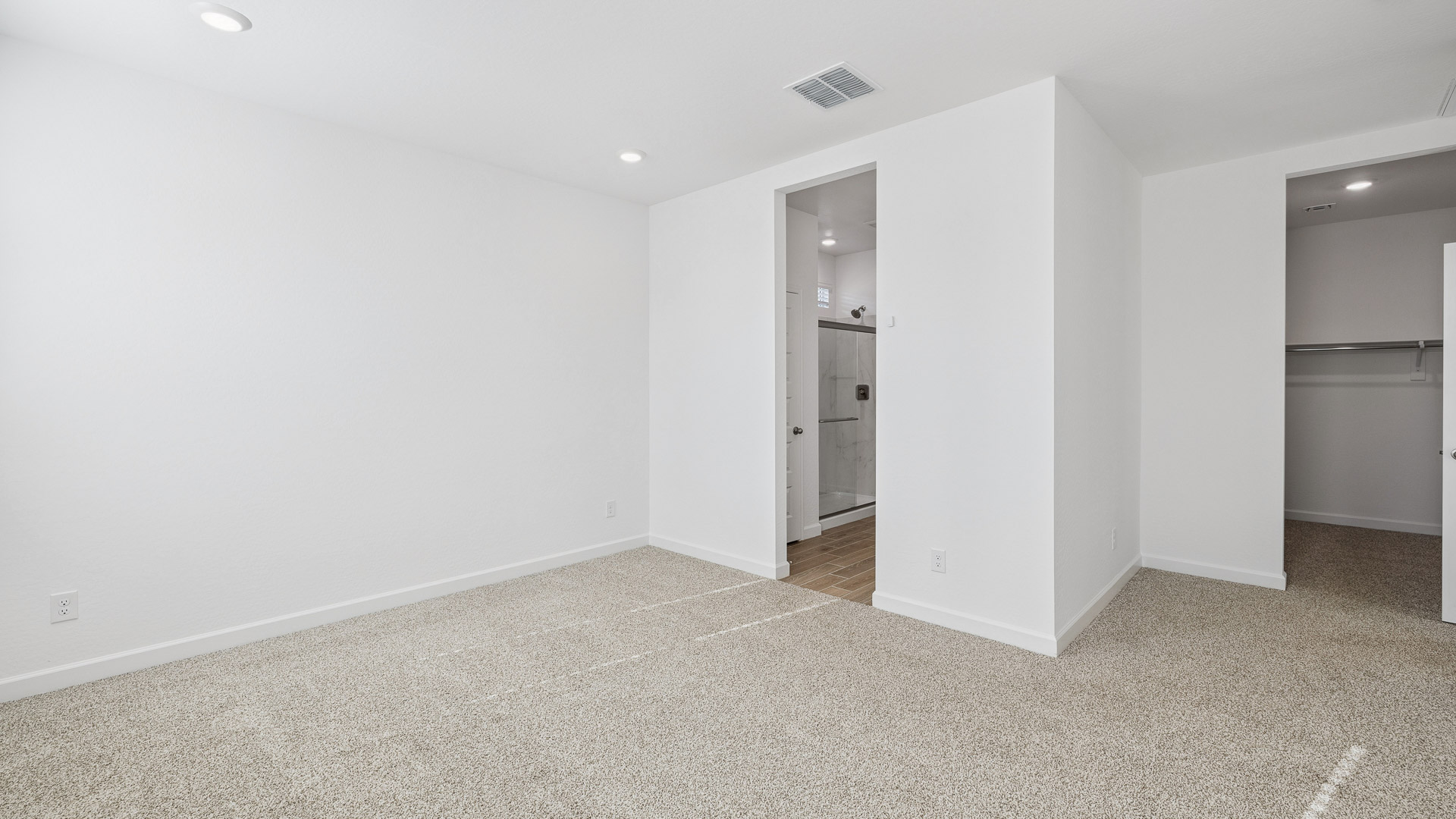 Primary bedroom with ceiling fan, plush carpeting, and a large walk-in closet.