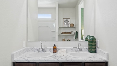 Modern primary bathroom with double vanities, porcelain countertops with a walk-in shower and a walk-in closet.