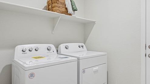 Spacious laundry room with washer and dryer connections and shelving for storage.