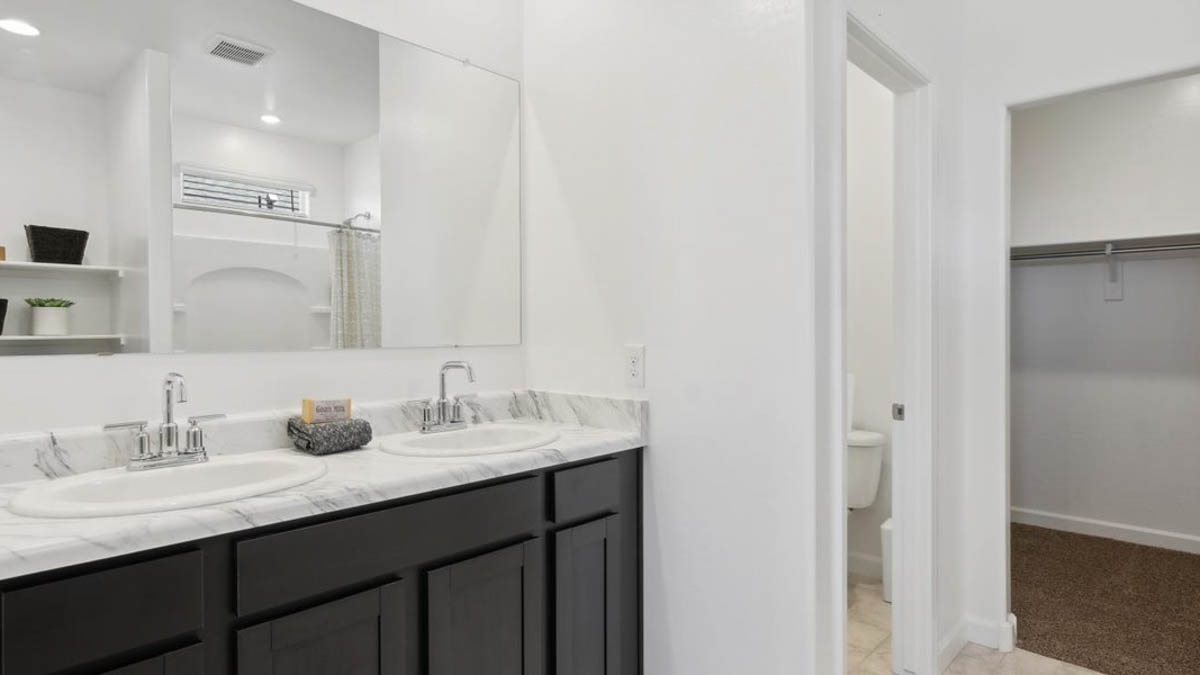 Modern primary bathroom with double vanities, porcelain countertops with a walk-in shower and a walk-in closet.