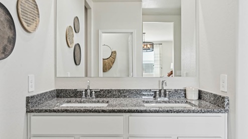Modern primary bathroom with double vanities, granite countertops with a walk-in shower and a walk-in closet.