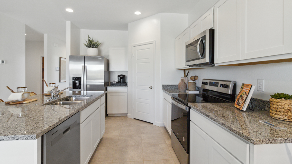 Side kitchen view showing pantry, island with sink, cabinets, and the appliance suite included Heartland Ranch