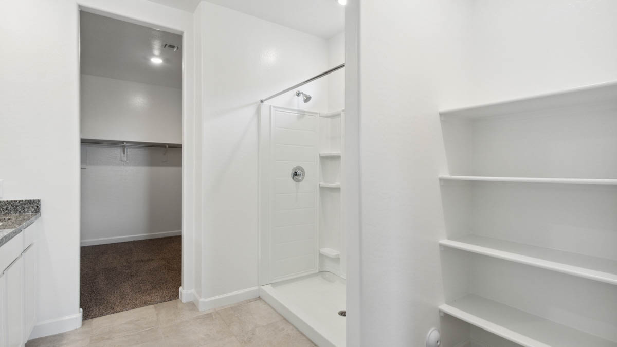 Modern primary bathroom with double vanity, granite countertops with a walk-in shower and a walk-in closet.