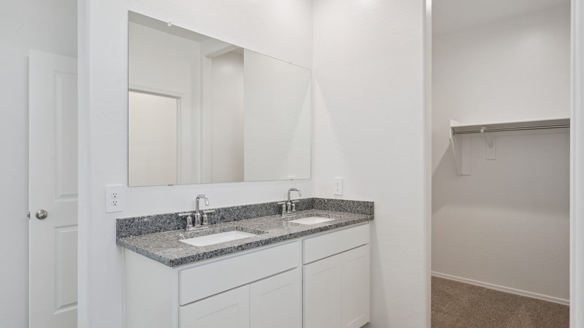 Modern primary bathroom with double vanity, granite countertops with a walk-in shower and a walk-in closet.