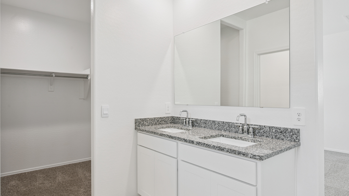 Modern primary bathroom with double vanity, granite countertops with a walk-in shower and a walk-in closet.