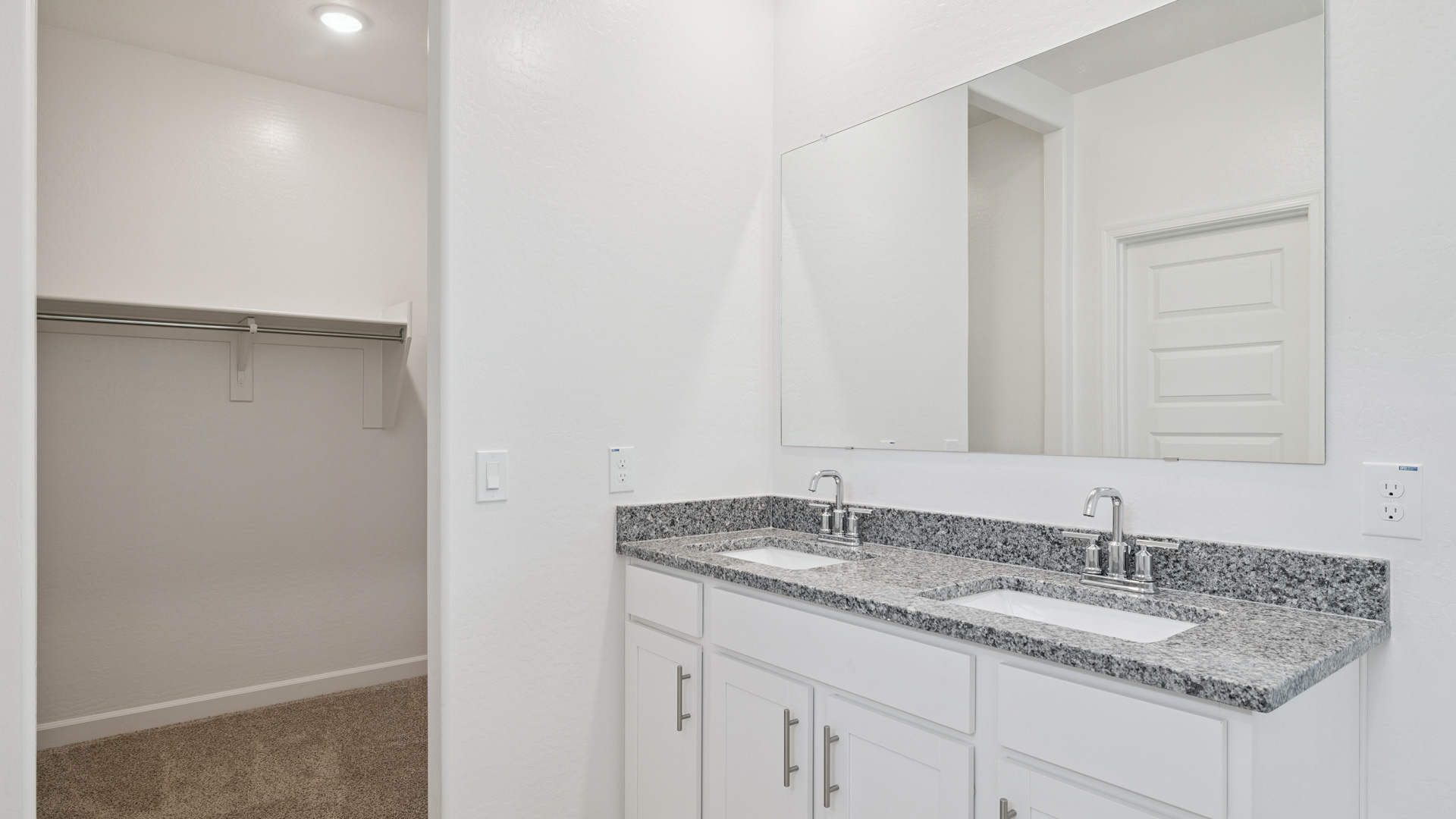 Modern primary bathroom with double vanity, granite countertops with a walk-in shower and a walk-in closet.