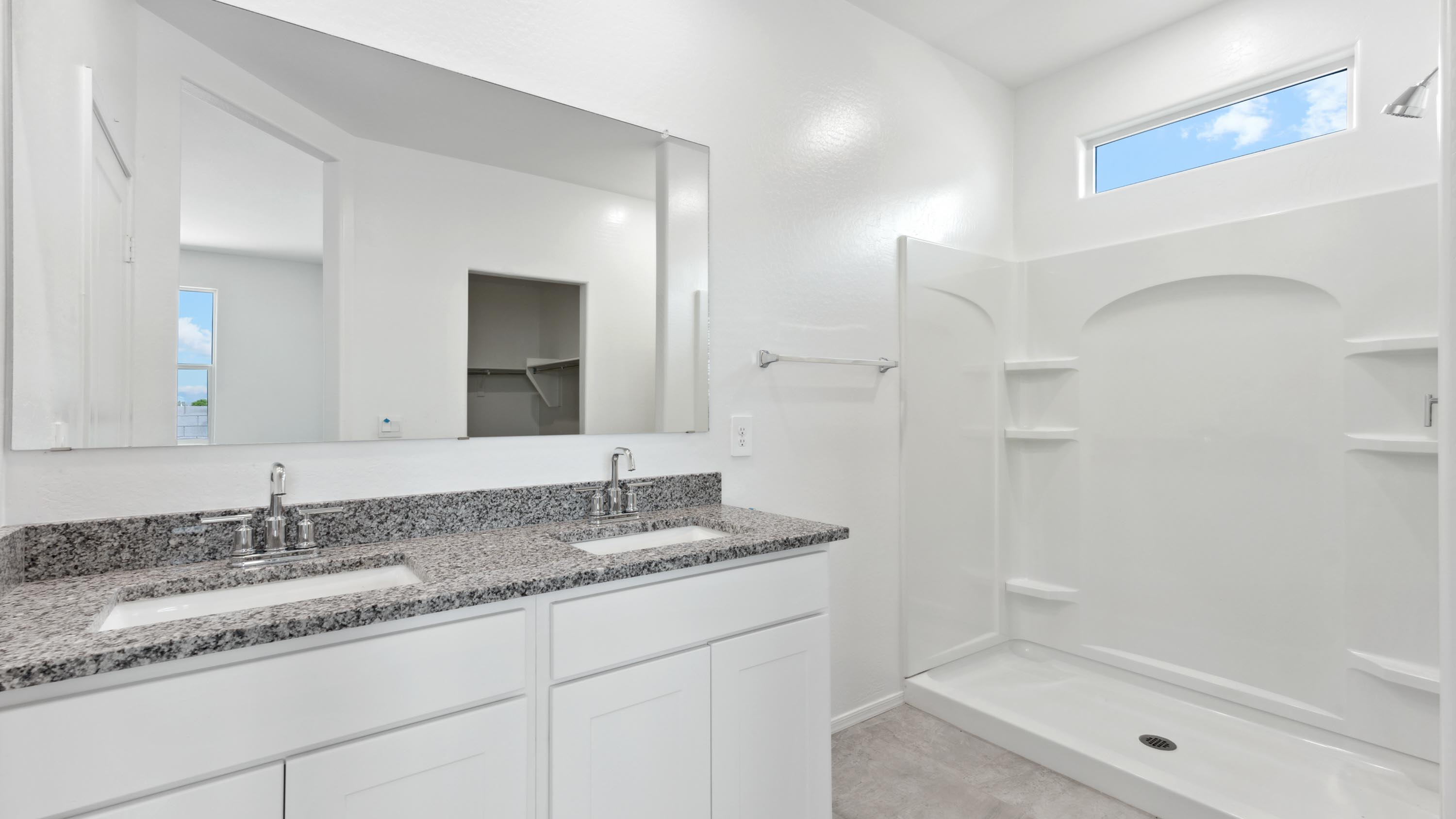 Modern primary bathroom with double vanity, granite countertops with a walk-in shower and a walk-in closet.