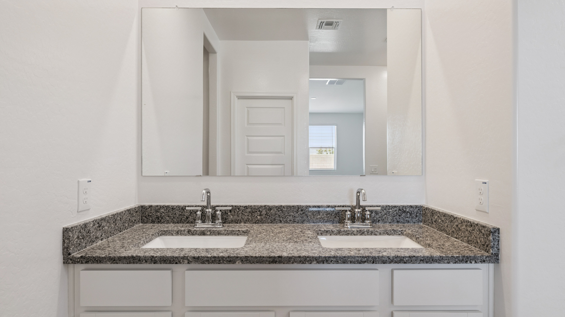 Modern primary bathroom with double vanity, granite countertops with a walk-in shower and a walk-in closet.