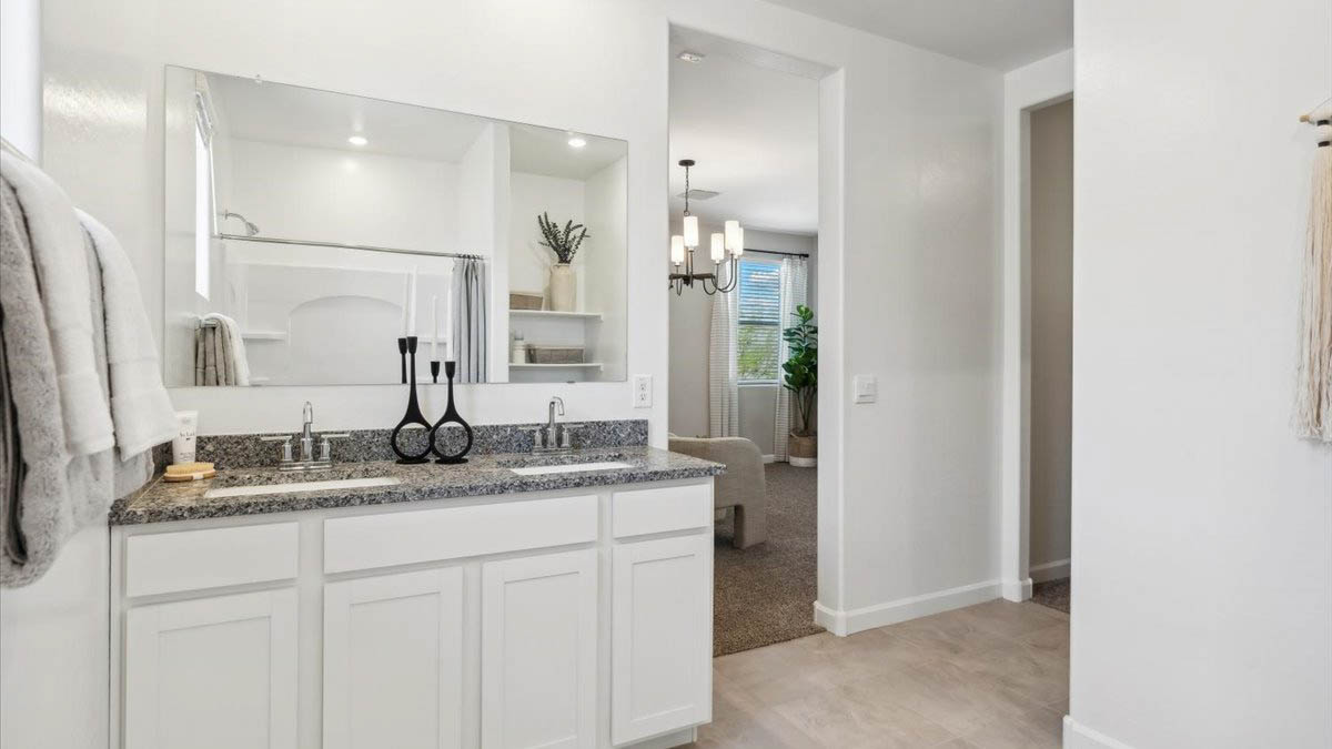 Modern primary bathroom with double vanity, granite countertops with a walk-in shower and a walk-in closet.