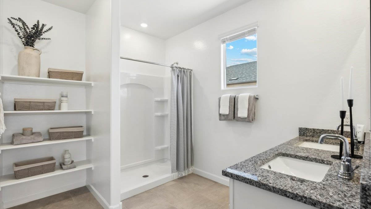 Modern primary bathroom with double vanity, granite countertops with a walk-in shower and a walk-in closet.