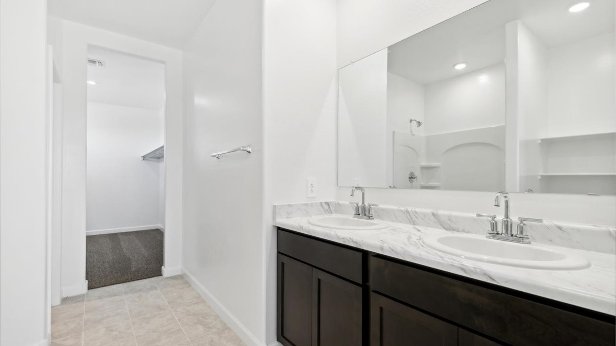 Modern primary bathroom with double vanities, porcelain countertops with a walk-in shower and a walk-in closet.