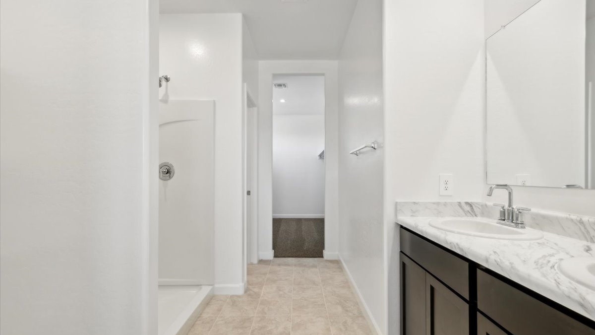 Modern primary bathroom with double vanities, porcelain countertops with a walk-in shower and a walk-in closet.